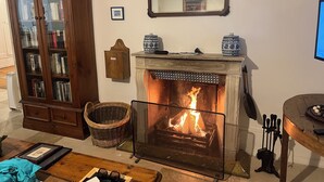 A cozy living room with a fireplace, a wooden cabinet with glass doors, a mirror, and a small table with decorative items.