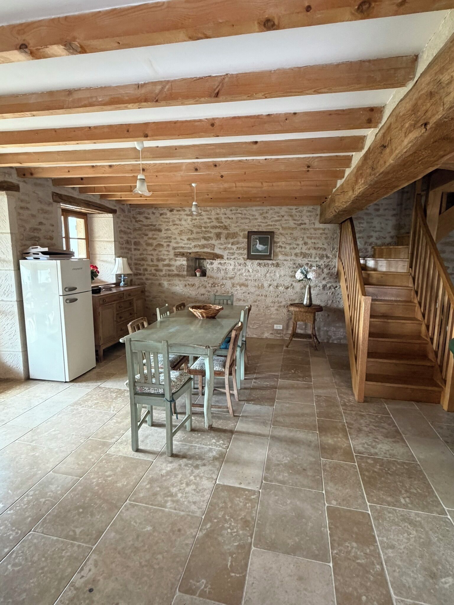 Un coin repas rustique avec un mur en pierre, des poutres en bois, un sol carrelé et un escalier.