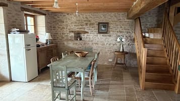 Un coin repas rustique avec un mur en pierre, des poutres en bois, un sol carrelé et un escalier.