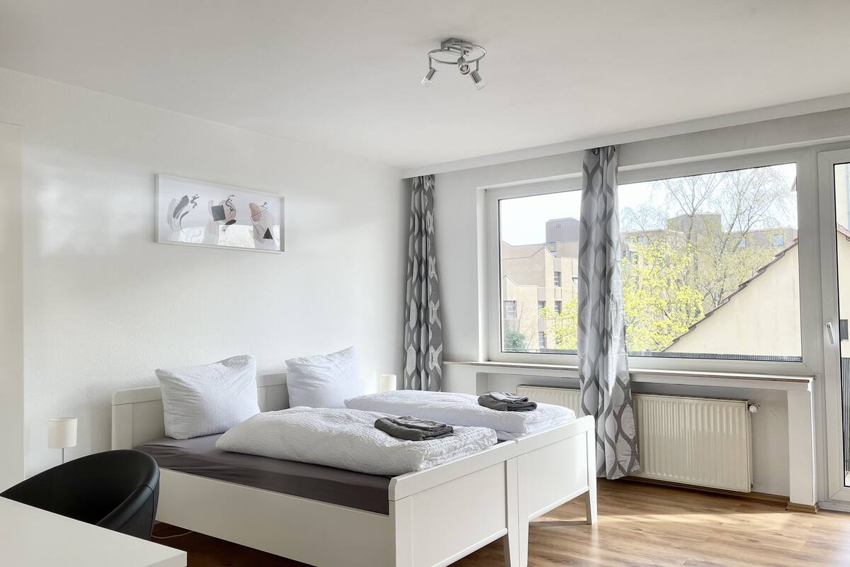 A modern bedroom with a bed, a desk, and a window with curtains.