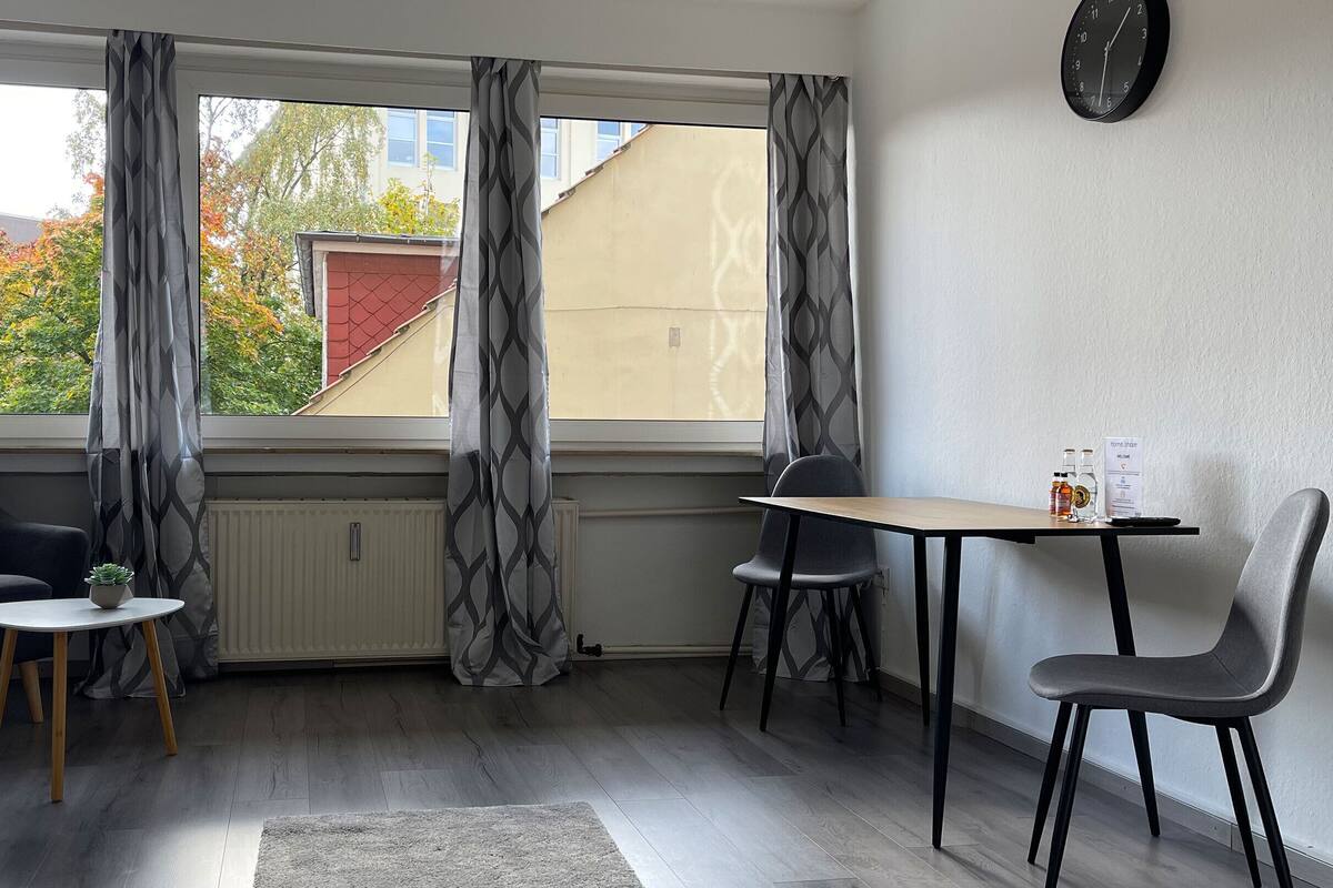 A room with a window, two chairs, a small table, and a clock on the wall.