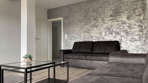 Un salon moderne avec un canapé d’angle gris, une table basse en verre et une petite plante en pot.