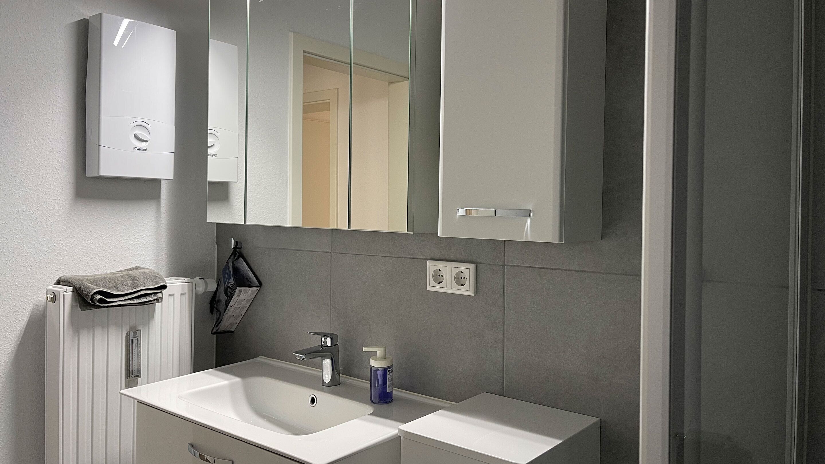 Un baño con un lavabo blanco, un espejo y un perchero para toallas.