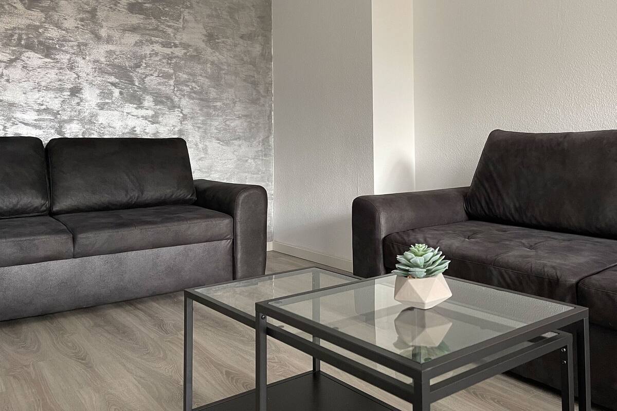 A modern living room with two dark leather sofas, a glass coffee table, and a textured wall.