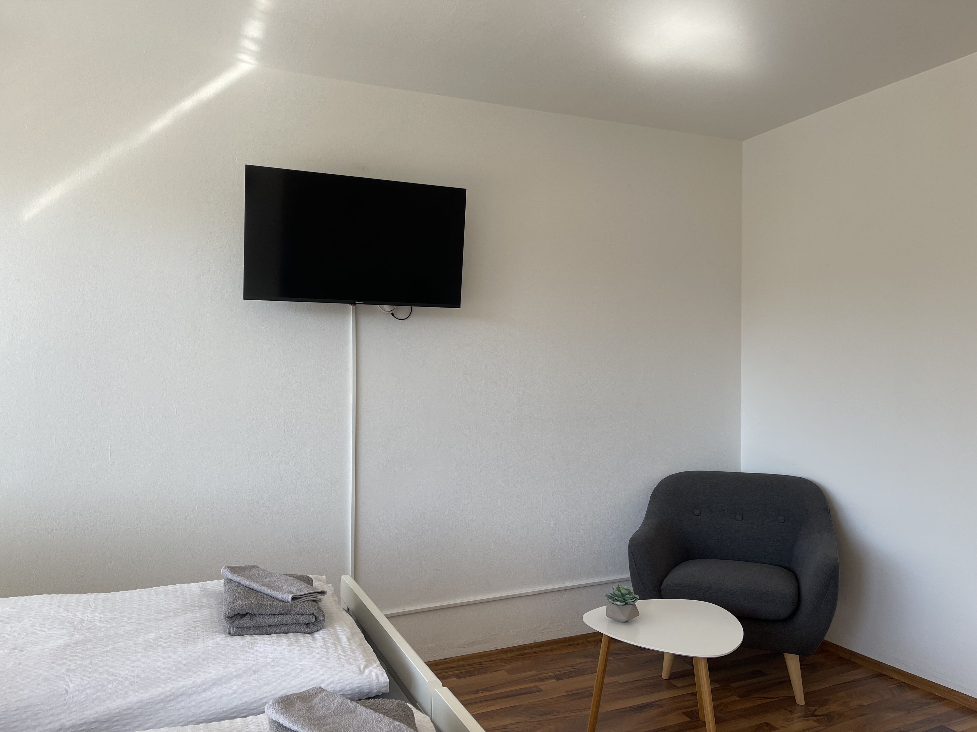 Une pièce comprenant un lit, une chaise, une petite table et un téléviseur fixé au mur.