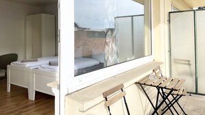 Une chambre avec une grande fenêtre, un lit, une chaise et une petite table.