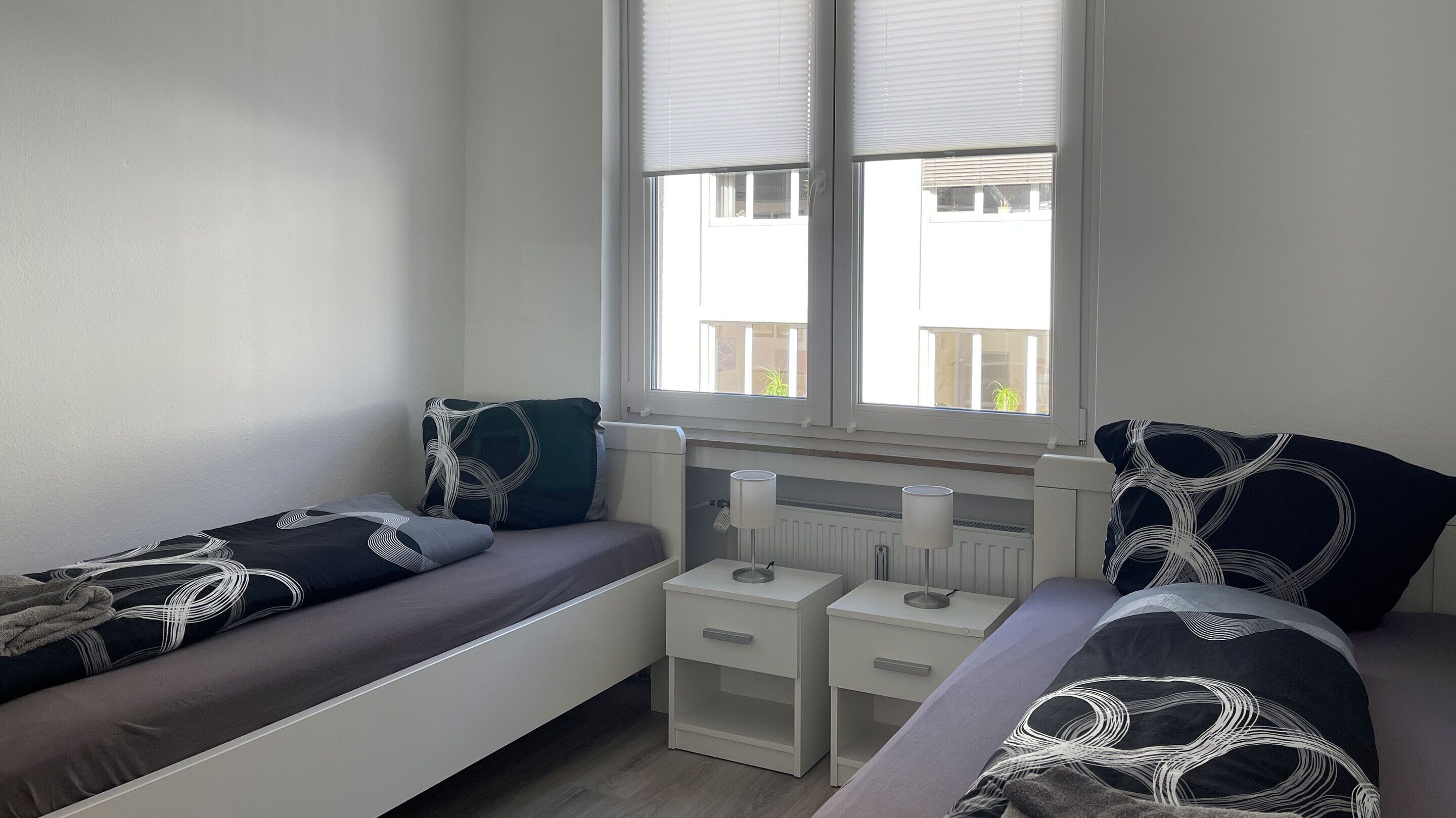 A bedroom with two single beds, a radiator, and a window with blinds.