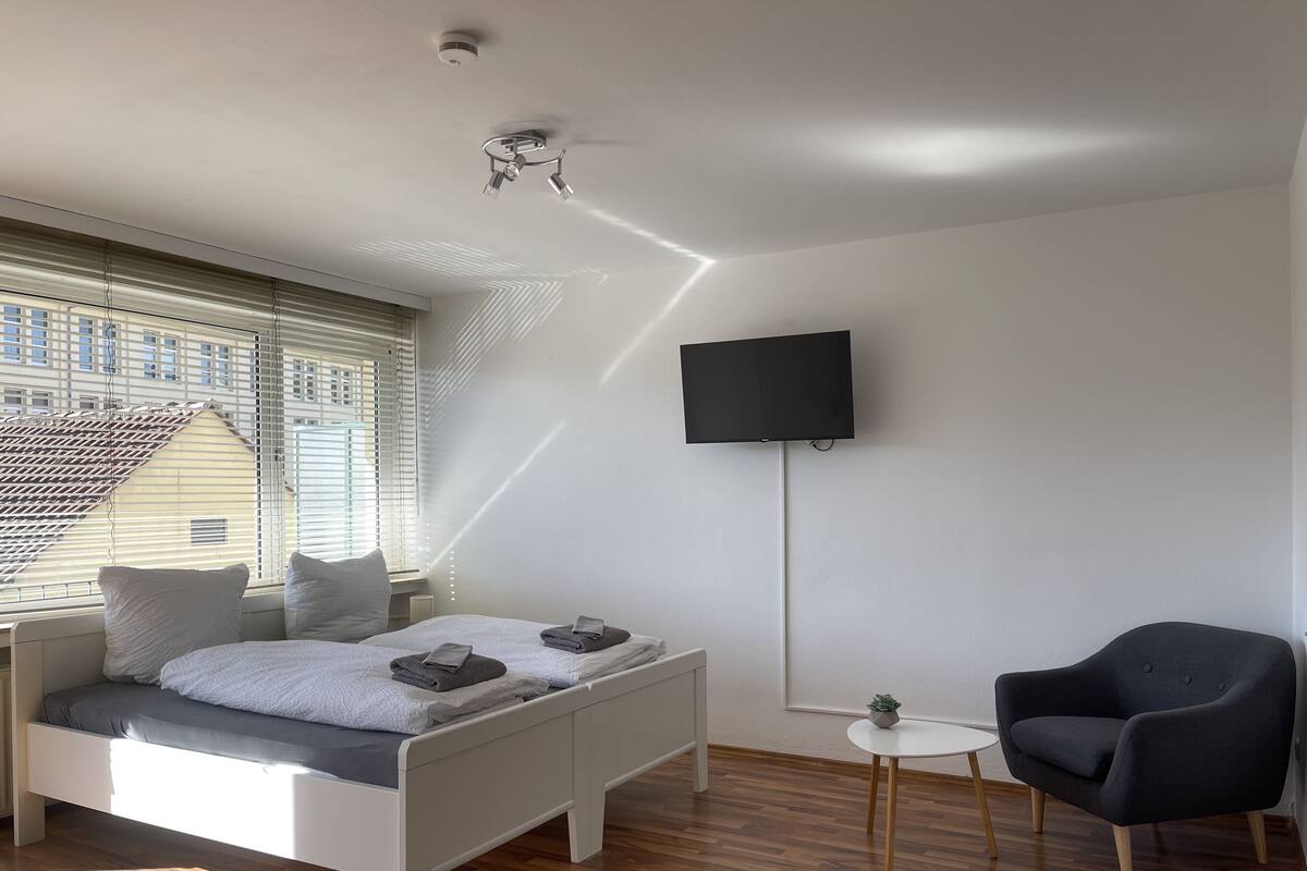 A modern bedroom with a bed, a TV, a chair, and a small table.