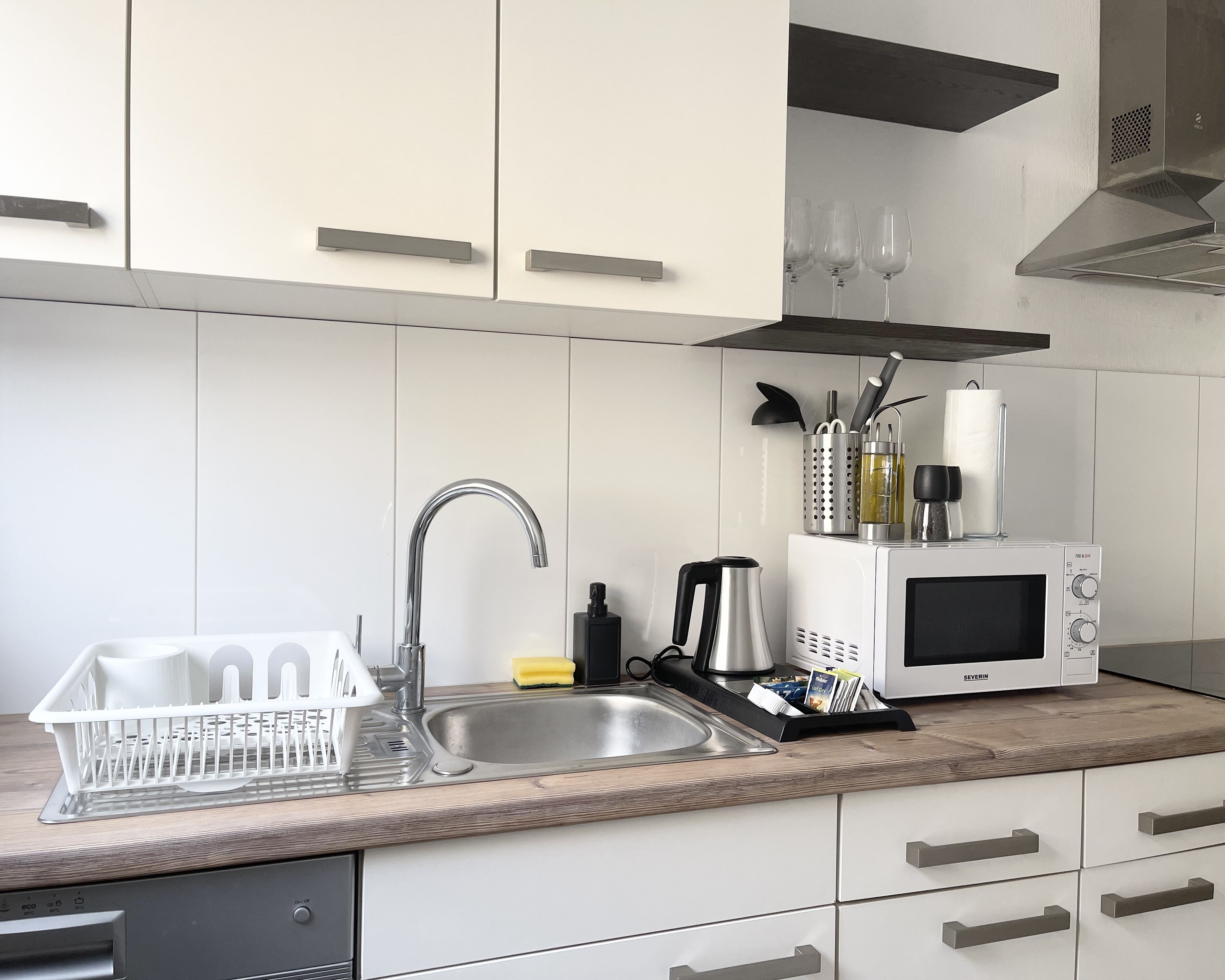 A modern kitchen with a stainless steel sink, a microwave, and a dish rack.