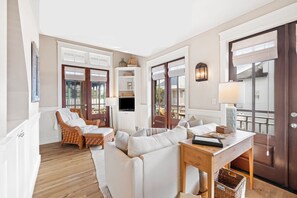 A living room with a sofa, chairs, a TV, a table, and a door with a view.