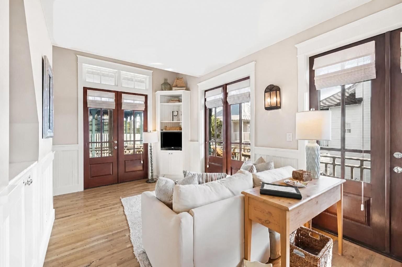 Un amplio salón con sofá, una mesa de madera y televisor. Hay ventanas grandes y vistas al exterior.