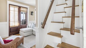 Una escalera de madera con barandilla que conduce a un rellano con una puerta blanca y un banco acolchado blanco.