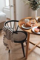A dining table with a croissant, a glass of water, and a cup. A chair with a striped towel is next to the table.