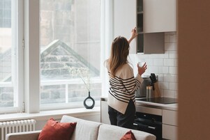 A woman in a kitchen with a view of a stone building outside.