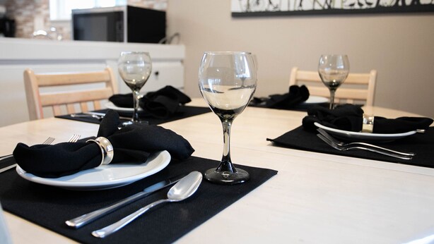 Una mesa de comedor con platos, cubiertos y copas de vino, con un posavasos y servilleta negros.