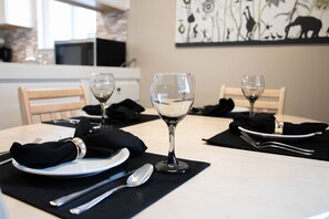 Una mesa de comedor con platos, cubiertos y copas de vino, con un posavasos y servilleta negros.