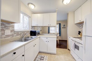 A modern kitchen with white cabinets, a stainless steel sink, a microwave, and a stove.