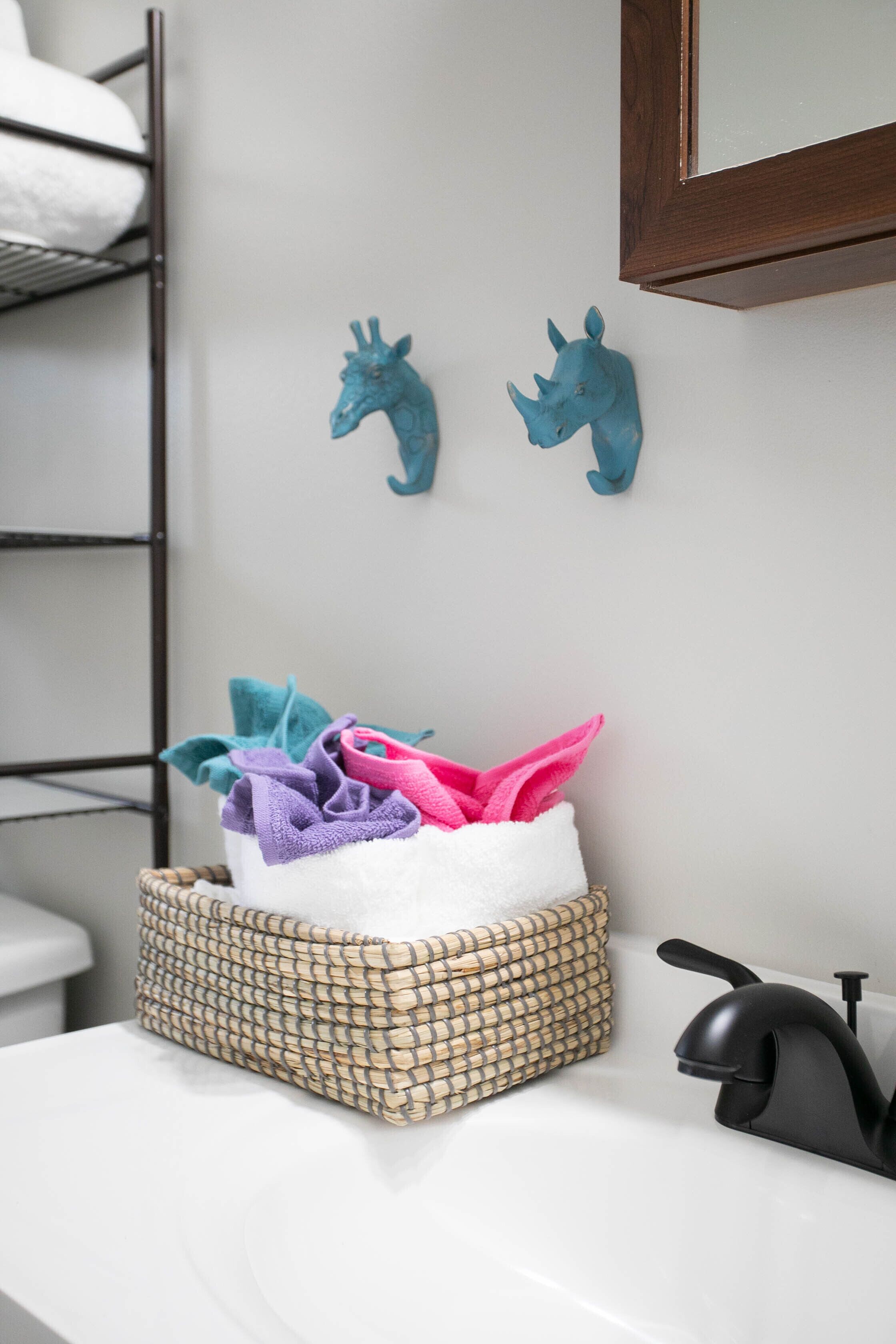 A bathroom with a woven basket containing colorful towels, a black faucet, and two blue wall decorations.