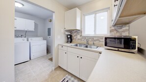 Una cocina con armarios blancos, microondas, lavabo y zona de lavandería.