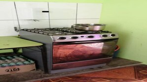 A kitchen with a gas stove, a stainless steel pot on the burner, and a box labeled "ZIR" on the floor. - Puriq wasi (Socabaya)