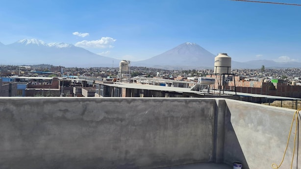 A rooftop with a water tank and a view of a cityscape with a mountain in the background. - Puriq wasi (Socabaya)