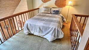 Ein Schlafzimmer mit einem Bett, einem Holgeländer, einer Lampe und zwei gewebten Wanddekorationen.