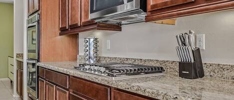 A kitchen with wooden cabinets, a stainless steel microwave, a gas stove, and a knife block.