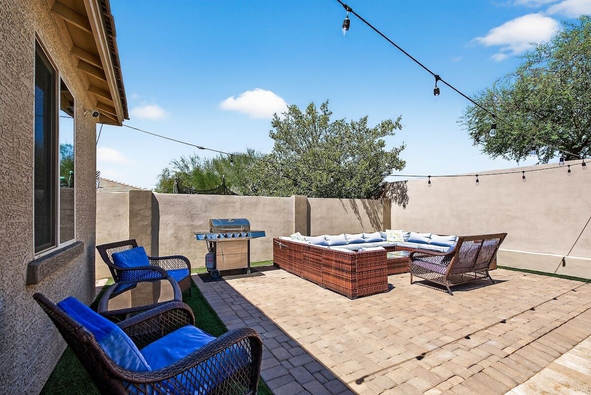 An outdoor patio with wicker furniture, a grill, and string lights.