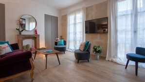 A living room with a fireplace, a TV mounted on the wall, and a large window with sheer curtains. - Flamingo Duplex, historical centre, l'Hauture, Arles (Arles)