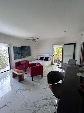 A modern living room with a bed, red sofas, a dining table, and a ceiling fan.