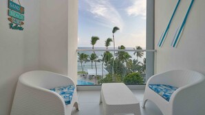 Un balcon doté de meubles en osier blancs, une vue sur la plage et une pancarte indiquant : « SAND BEACH SURF, détente garantie ».