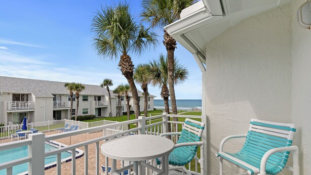 A balcony with a pool, white furniture, and palm trees.