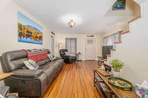 A living room with a leather sofa, a wooden coffee table, and a painting of a landscape. - Katahdin Comfort - A Beautiful Four Bedroom Home (Millinocket)