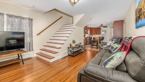 Un salon moderne avec un escalier en bois, un canapé en cuir, un téléviseur à écran plat et un coin repas doté de meubles de rangement en bois.