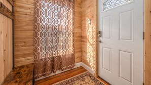 L’intérieur d’un chalet en bois, avec une porte blanche, un rideau à motifs et un plancher en bois.