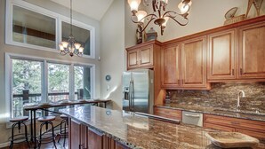Una cocina amplia con armarios de madera, encimera de granito, refrigerador de acero inoxidable y una barra con taburetes.