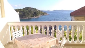A balcony with a table and chairs, overlooking a body of water and a green hillside.