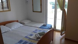 A bedroom with two single beds, a window with curtains, and a view of the outdoors.