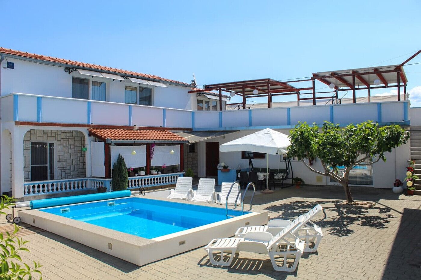 A two-story building with a swimming pool, outdoor seating, and a covered patio area.