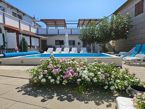 Une piscine avec des chaises longues, une pergola et un parterre de fleurs.
