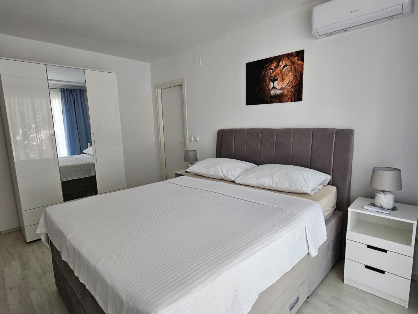 A modern bedroom with a bed, a nightstand, a lamp, and a wall-mounted air conditioner.