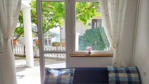 Une pièce avec un canapé bleu, une fenêtre donnant sur un paysage verdoyant et un vase rempli de fleurs posé sur le rebord de la fenêtre.