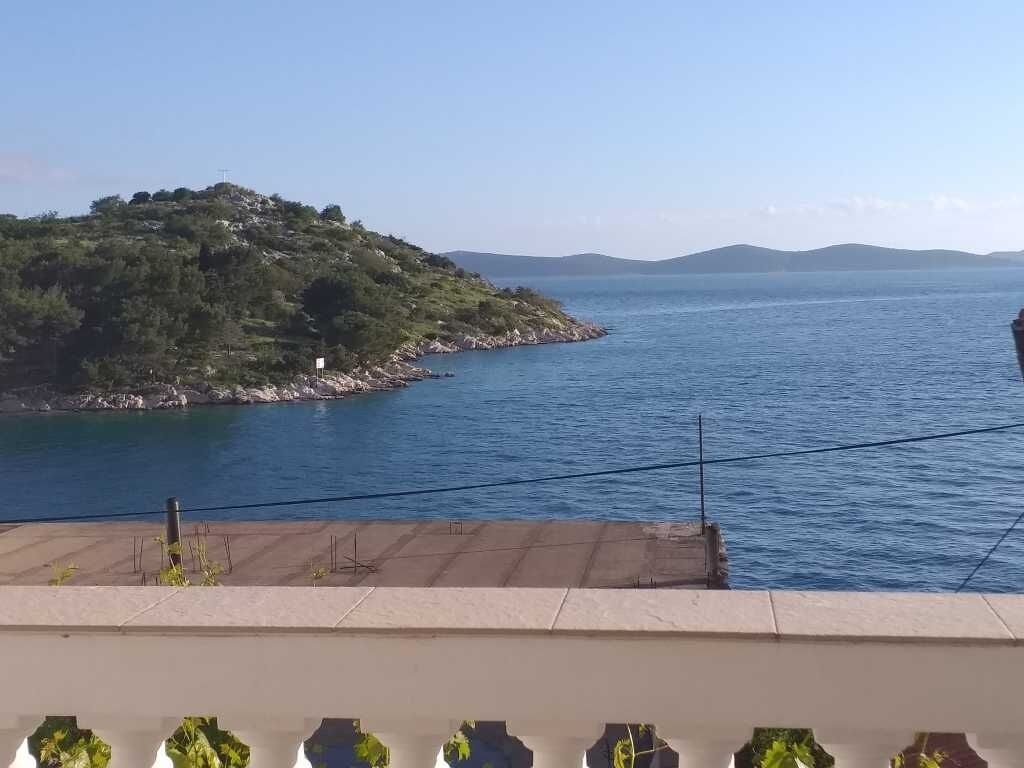 A coastal view with a clear sky, a rocky shoreline, and a distant mountain range.