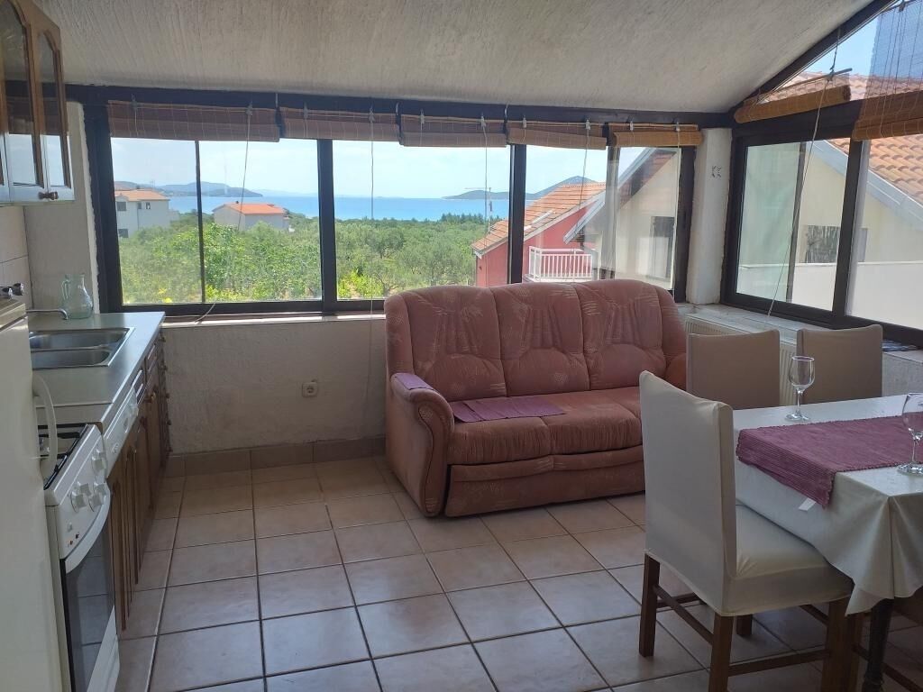 Ein Zimmer mit einer Küchenzeile, einem Sofa, einem Esstisch und Blick auf das Meer und die grüne Landschaft.
