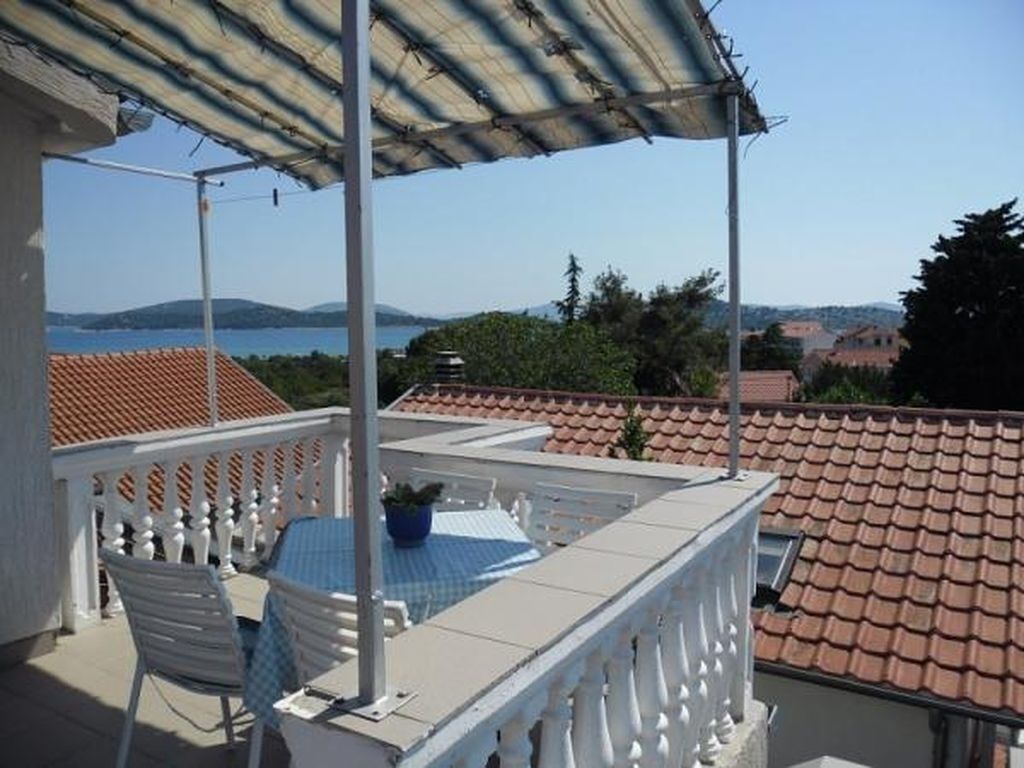 Ein Balkon mit Tisch und Stühlen, Blick auf das Meer und im Hintergrund rote Ziegeldächer.