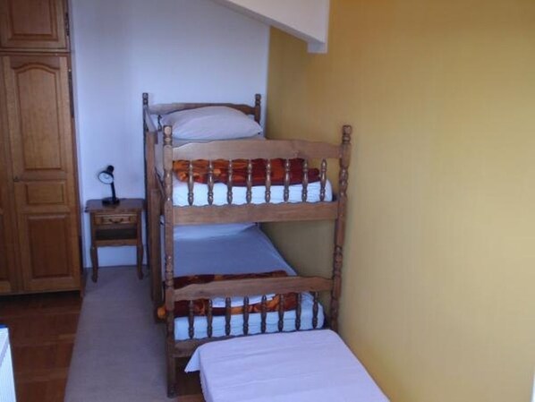 A bunk bed with two levels, a wooden wardrobe, and a small bedside table with a lamp.