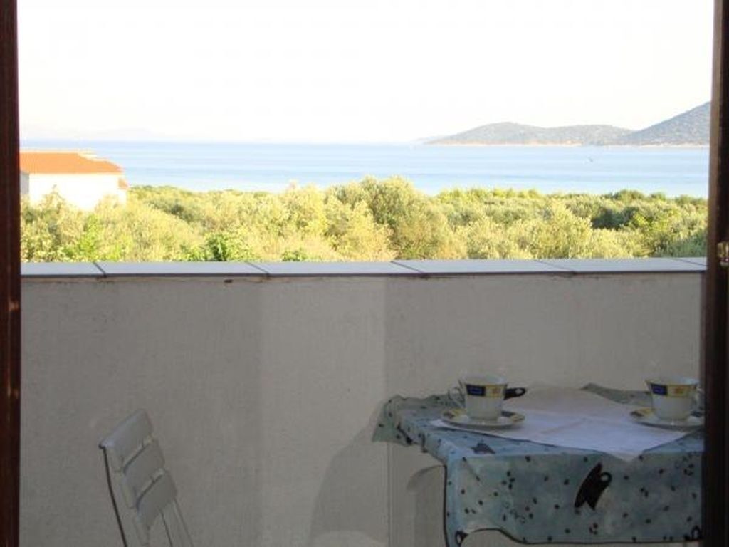 Ein Balkon mit Tisch und Stühlen, der auf eine Küstenlandschaft mit Grünflächen und Meerblick blickt.