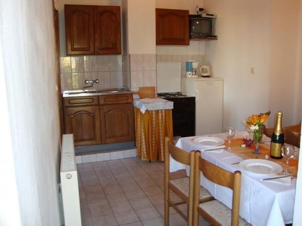 Cocina compacta con armarios de madera, una mesa de comedor para dos personas y un refrigerador pequeño.
