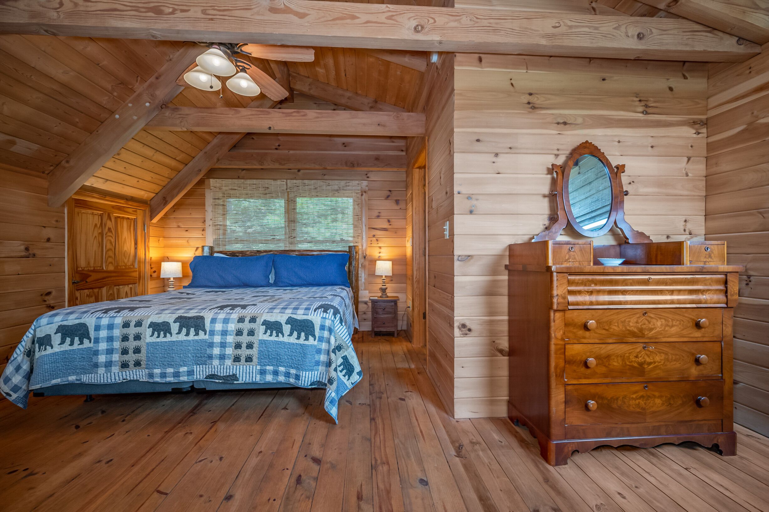 A cozy wooden cabin bedroom with a bed, dresser, and a mirror.