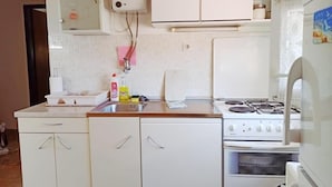Une cuisine de taille réduite avec des meubles blancs, une cuisinière à gaz et un réfrigérateur.